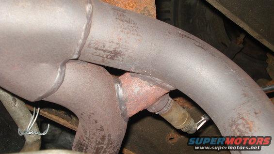 Close-up of a vehicle's exhaust pipe with an oxygen sensor attached. Some rust is visible