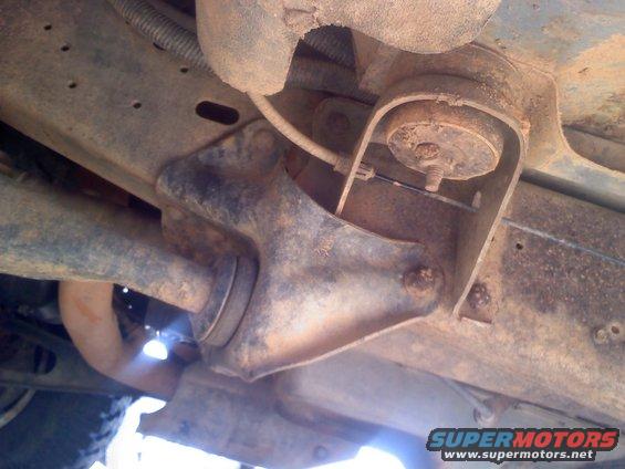 Underside view of rusty vehicle suspension parts, including a bracket and a shock absorber mount