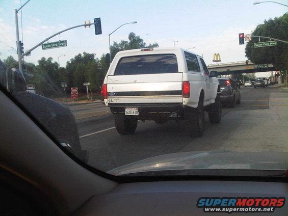 White Ford Bronco with a camper shell, lifted, seen from behind
