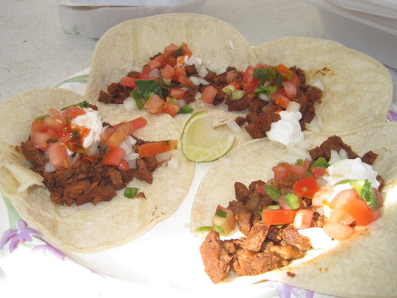 Four tacos with meat, pico de gallo, and crema on tortillas, with a lime wedge