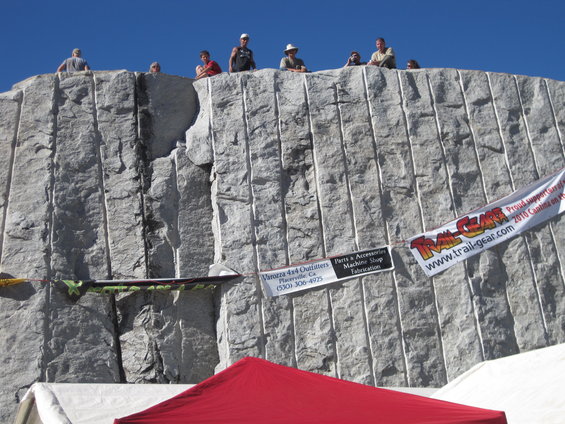 People stand atop a large, carved stone wall; banners hang on the wall
