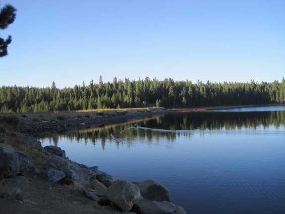Lake with trees and a person rowing a boat. Rocks in foreground