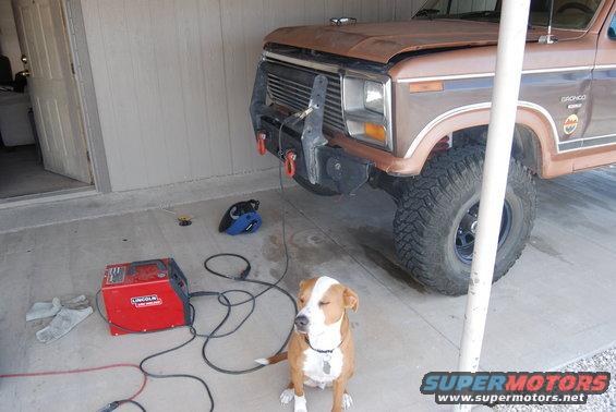 Brown Ford Bronco with aftermarket bumper, welding machine, and a dog sitting in front