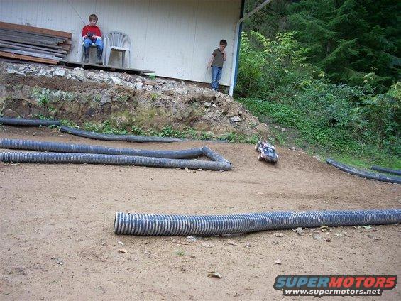 Remote control car on a dirt track with large corrugated pipes. Two boys watch