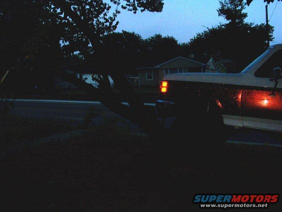White and brown truck with amber turn signal and red brake light illuminated. Appears to be a 1987-1991 Ford F-Series truck
