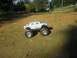 1994 Ford Escort - A remote-controlled monster truck sits on a dirt path with trees and a fence in the background.
