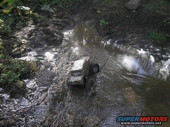 Toy truck in mud puddle, side view, with visible "SUPERMOTORS" text on lower right