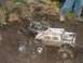 1994 Ford Escort - Remote control trucks are stuck in a muddy terrain with rocks and vegetation.