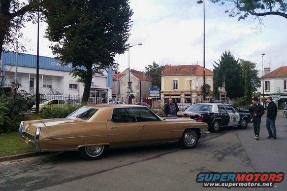 Tan 1970s Cadillac Coupe de Ville parked next to a police car