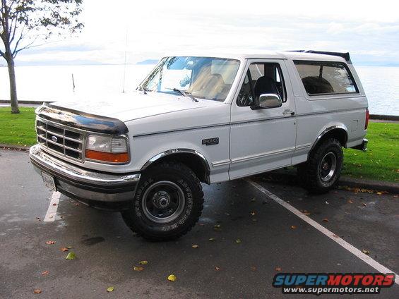 White 1995 Ford Bronco parked curbside with a water view