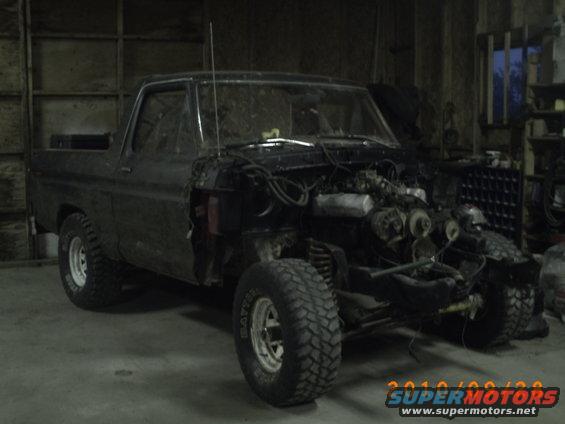 Dark colored Ford Bronco with front end disassembled in a garage. Engine is exposed