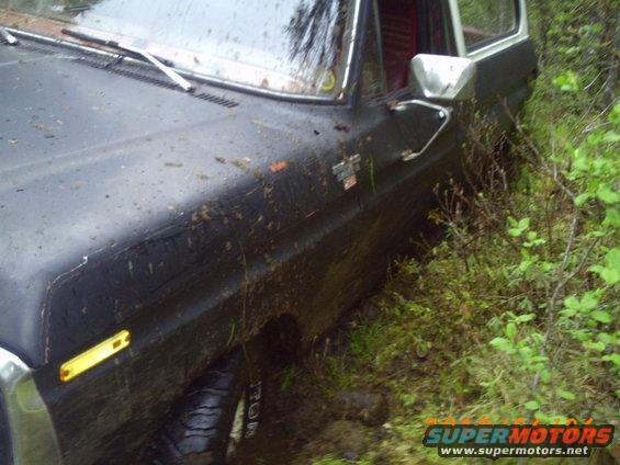Muddy 1970s Ford Bronco stuck in brush, driver's side front quarter visible
