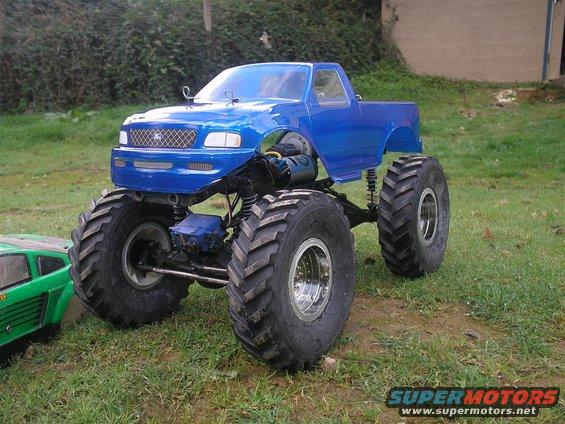 Blue RC monster truck with large tires, parked next to a green RC car