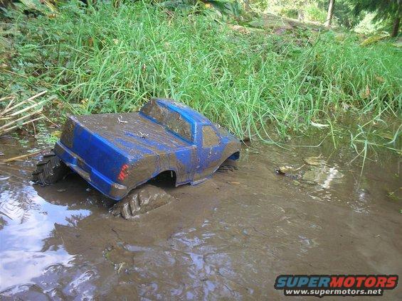 Blue RC truck body stuck in mud, rear view. Large tires visible