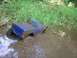 1994 Ford Escort - A blue remote-controlled truck body is stuck in muddy water with tall grass in the background.