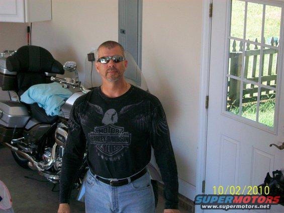 Man in a Harley-Davidson shirt stands in a garage next to a large touring motorcycle