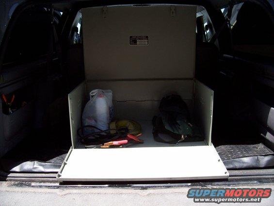 Open cargo box in vehicle interior with bags and jumper cables