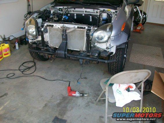 SUV front end disassembled, showing radiator and engine components, with a red drill on the floor