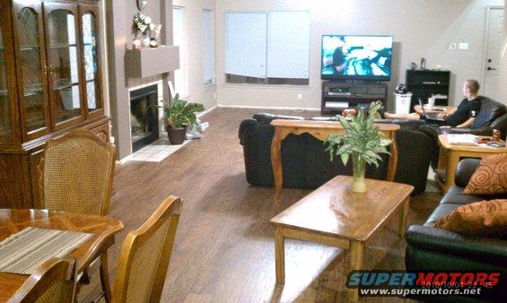 Living room with fireplace, dining set, sofas, and television showing a car