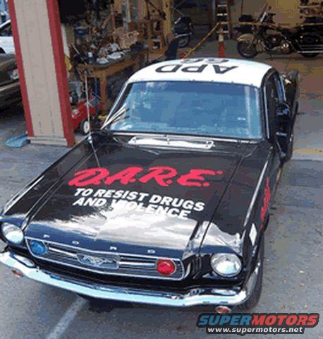 Black 1965 Mustang police car with D.A.R.E. logo on hood and 'APD' on roof