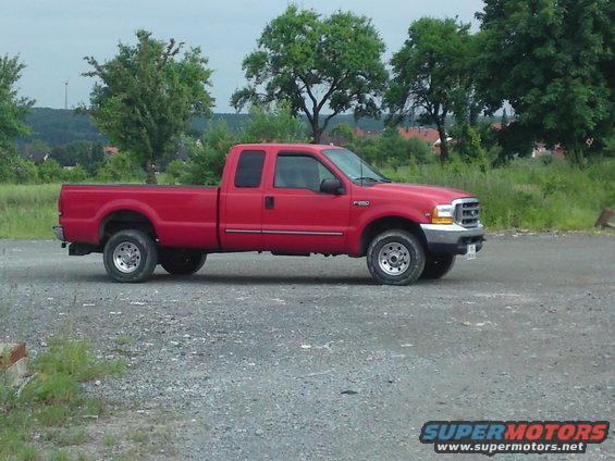 Red pickup truck, side view, parked on gravel lot