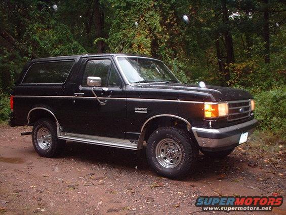 1989 Ford Bronco parked on a dirt road with trees in the background