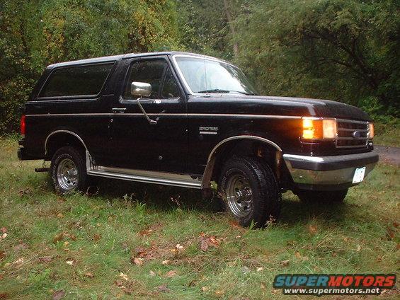 Black 1989 Ford Bronco parked on grassy area with trees in background