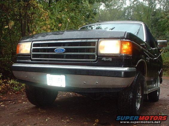 Front view of a black Ford F-series truck, likely 1987-1991 model year, with headlights on
