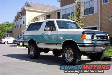 White and teal 1990 Ford Bronco with aftermarket wheels and tires, lifted suspension, and a bug deflector