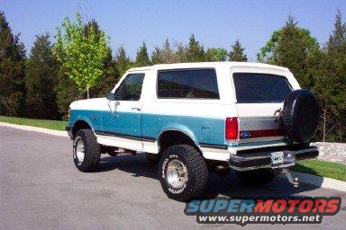 1990 Ford Bronco, two-tone white and blue, spare tire on rear door, parked on asphalt