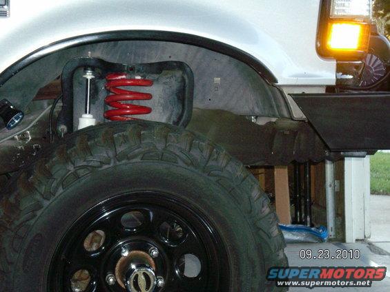 Close-up of a truck's front wheel well, showing a red coil spring and shock absorber