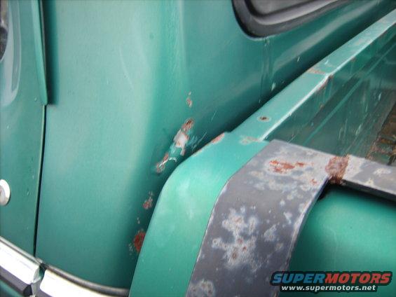 Close-up of a green truck fender with rust spots and a rusty metal trim piece