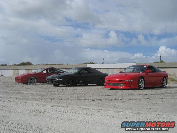 Three 1994 Ford Probe cars parked on sand with a cloudy sky