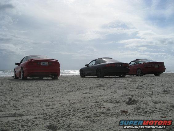 Three coupes parked on a sandy beach with the ocean in the background