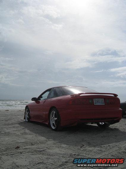 Red 1994 Ford Probe parked on a sandy beach with ocean waves in the background