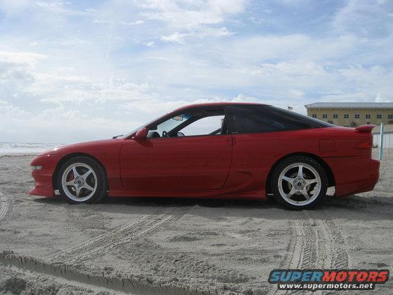 Red coupe with black roof and spoiler parked on a sandy beach with tire tracks
