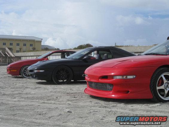 Red 1994 Ford Probe front view, parked on sand with two other cars