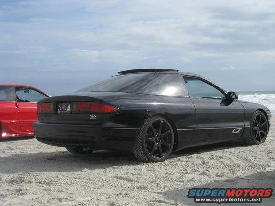 Black 1994 Ford Probe parked on sand with a red car behind it