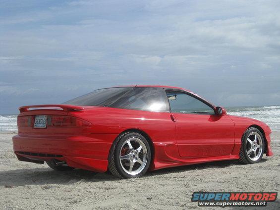 red 1994 Ford Probe parked on sand near ocean waves