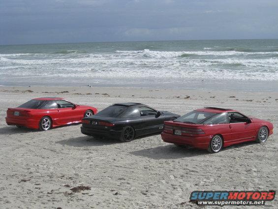 Three Ford Probe cars parked on a sandy beach with the ocean in the background