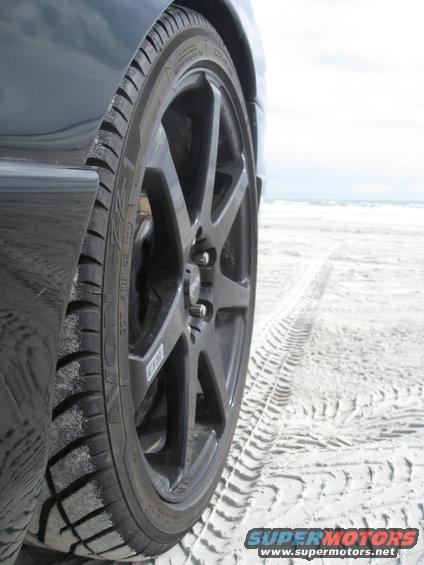 Black car wheel on beach with tire tracks