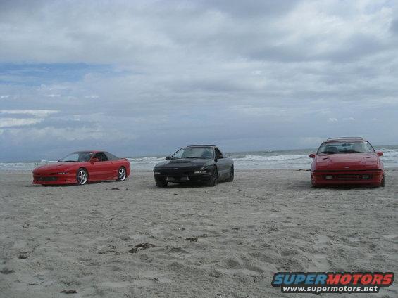 Three sports coupes parked on a sandy beach with the ocean in the background