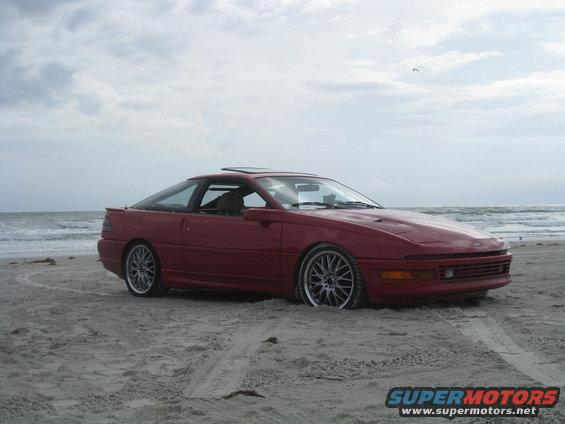 Red 1994 Ford Probe parked on a beach with the ocean in the background