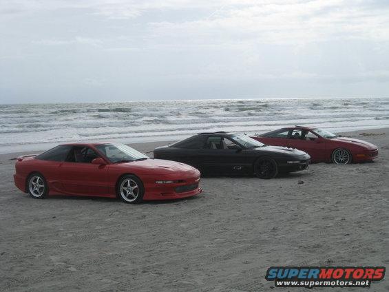 Three 1994 Ford Probes parked on a sandy beach with the ocean in the background