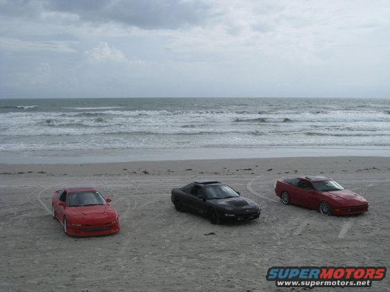 Three sports cars parked on a sandy beach with the ocean in the background