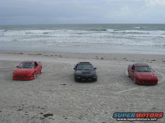 Three sports cars parked on a sandy beach with the ocean in the background