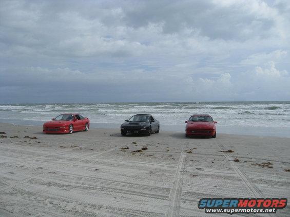 Three sports cars parked on a sandy beach with the ocean and cloudy sky in the background