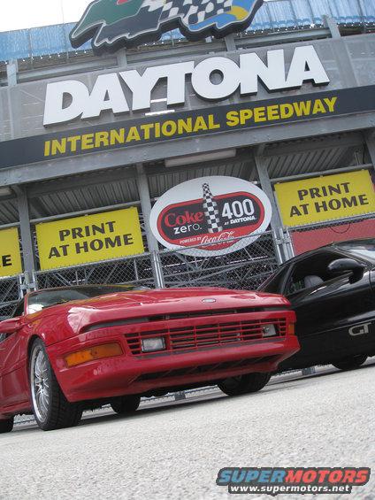 Red sports car front view at Daytona International Speedway with a black GT car behind it
