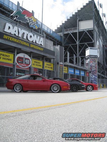 Red 1994 Ford Probe parked in front of Daytona International Speedway with two other cars