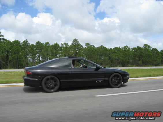 Black 1994 Ford Probe GT driving on a highway, side view. The car has black wheels and a sunroof